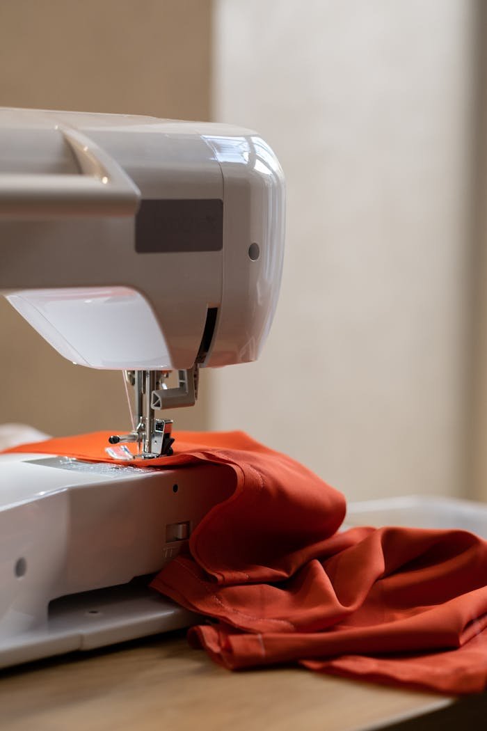 A sewing machine stitching orange fabric in a studio setting, showcasing fabric and craft.
